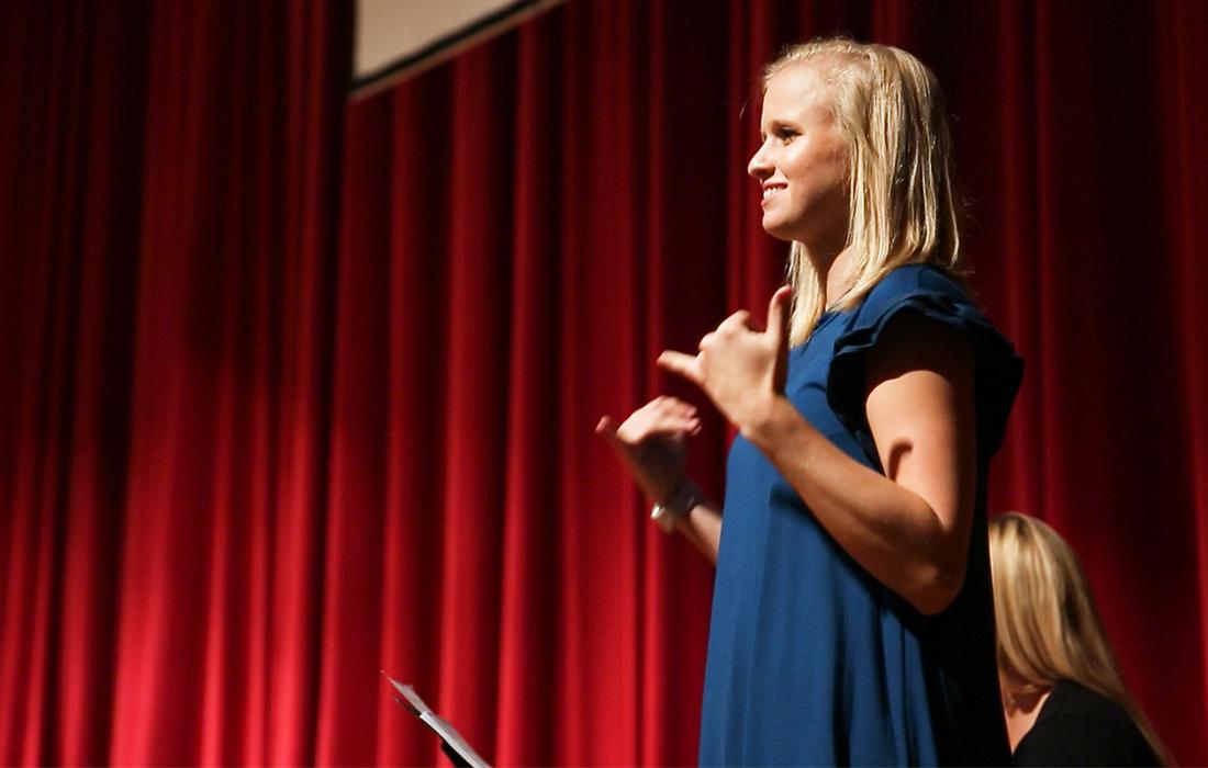 Female standing on stage, using sign language